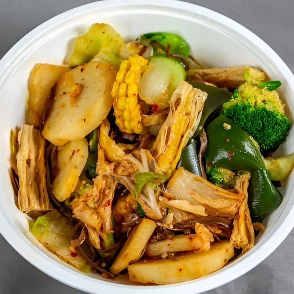 A close-up of a Chinese dish with broccoli, corn, tofu skin, and other vegetables in a white bowl.