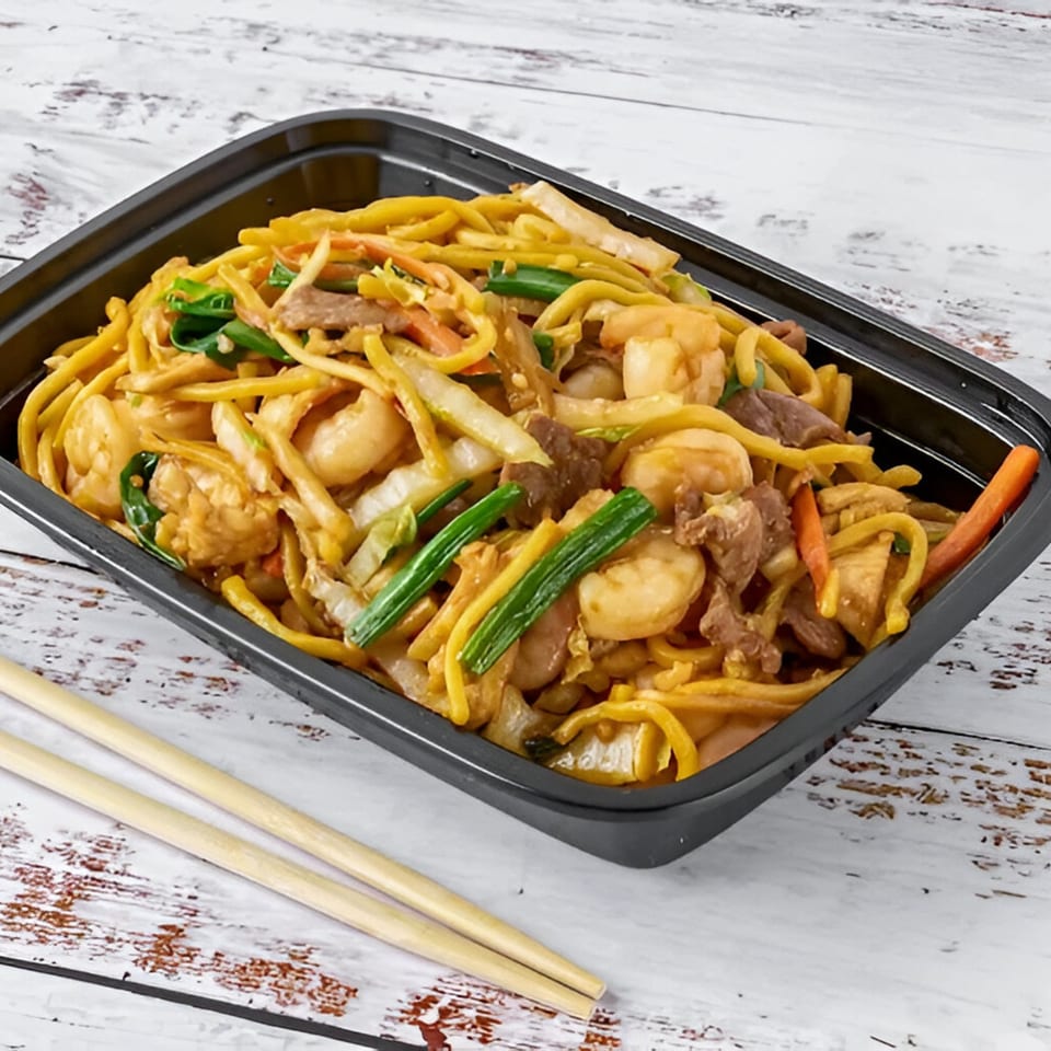 Red Wok's shrimp and beef lo mein with vegetables in a black takeout container with chopsticks.